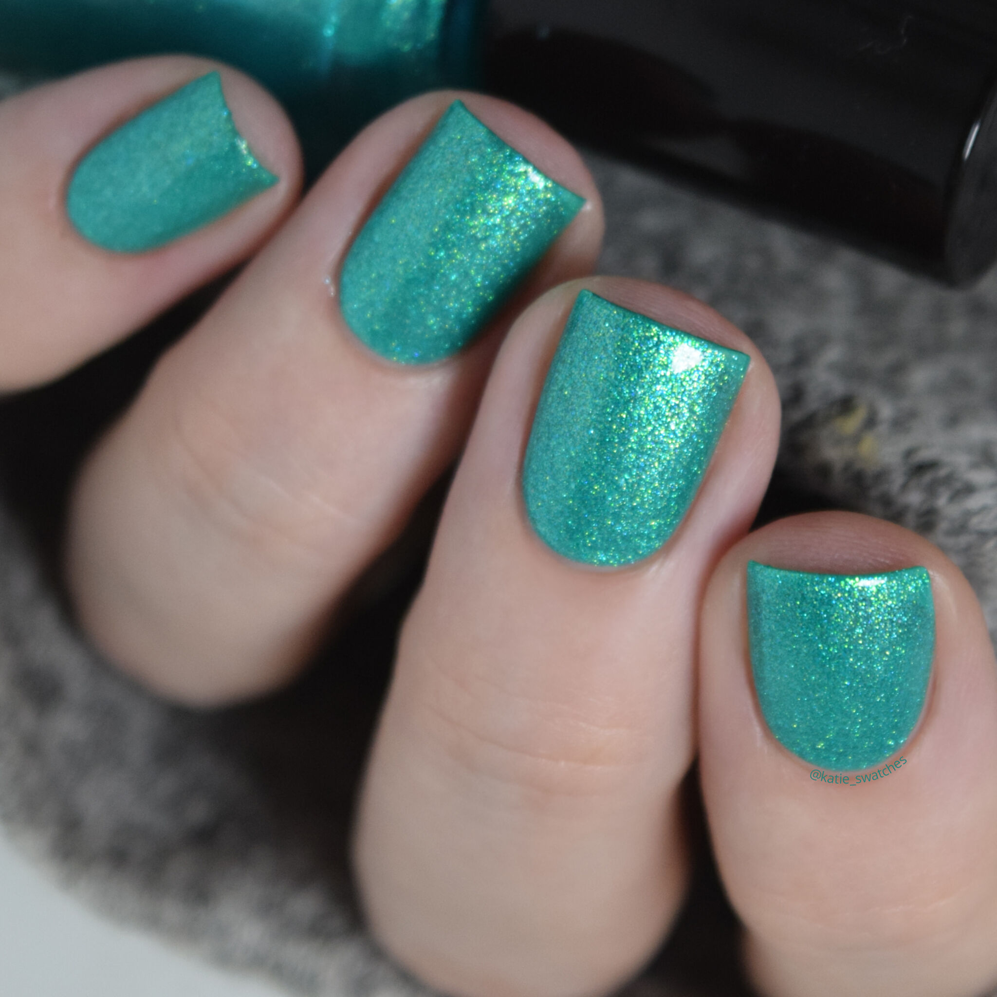 Girly Bits - Cross-Eyed Bear nail polish swatch with top coat. Caribbean green matte nail polish with a gold/blue shimmer.